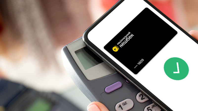 A person holds a smartphone displaying a Near Field Communication (NFC) payment app near a point-of-sale terminal, indicating a successful digital payment with a green checkmark on the screen.