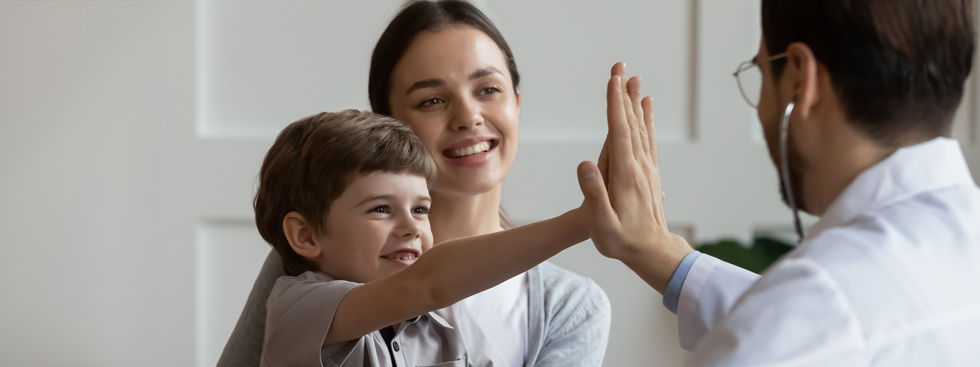 A child gives a high-five to a person in a white coat while a smiling woman watches.