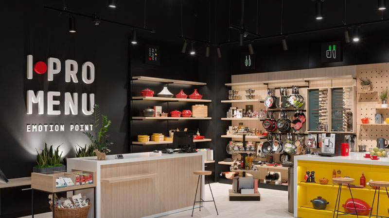 Modern kitchenware store with wooden displays, cookware on shelves, and a sign.