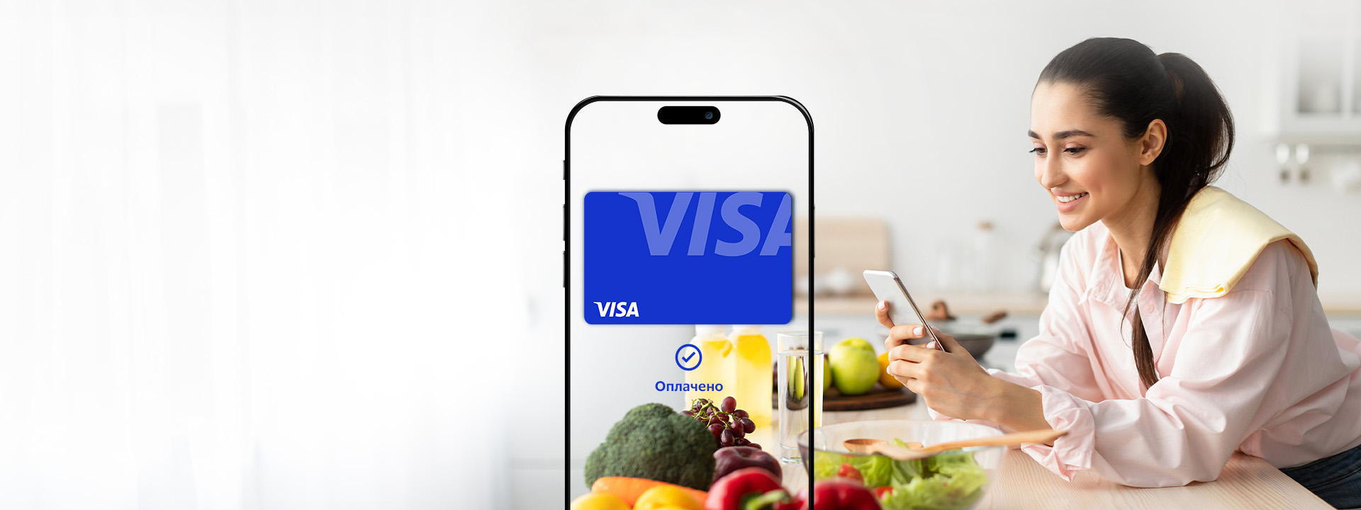 A person sitting at a white table filled with fruits and vegetables is holding a smartphone with a Visa advertisement displayed on the screen, symbolizing a digital transaction or online payment.