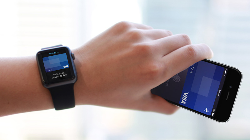 Hand holding a mobile phone with a Visa card on screen and an Apple watch on the wrist with a Visa card on screen.