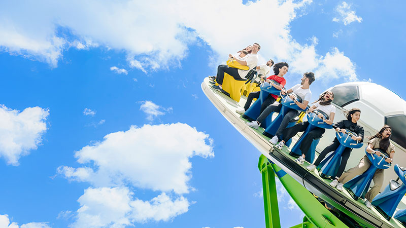 A group of people ride a large amusement park swing against a blue sky with scattered clouds.